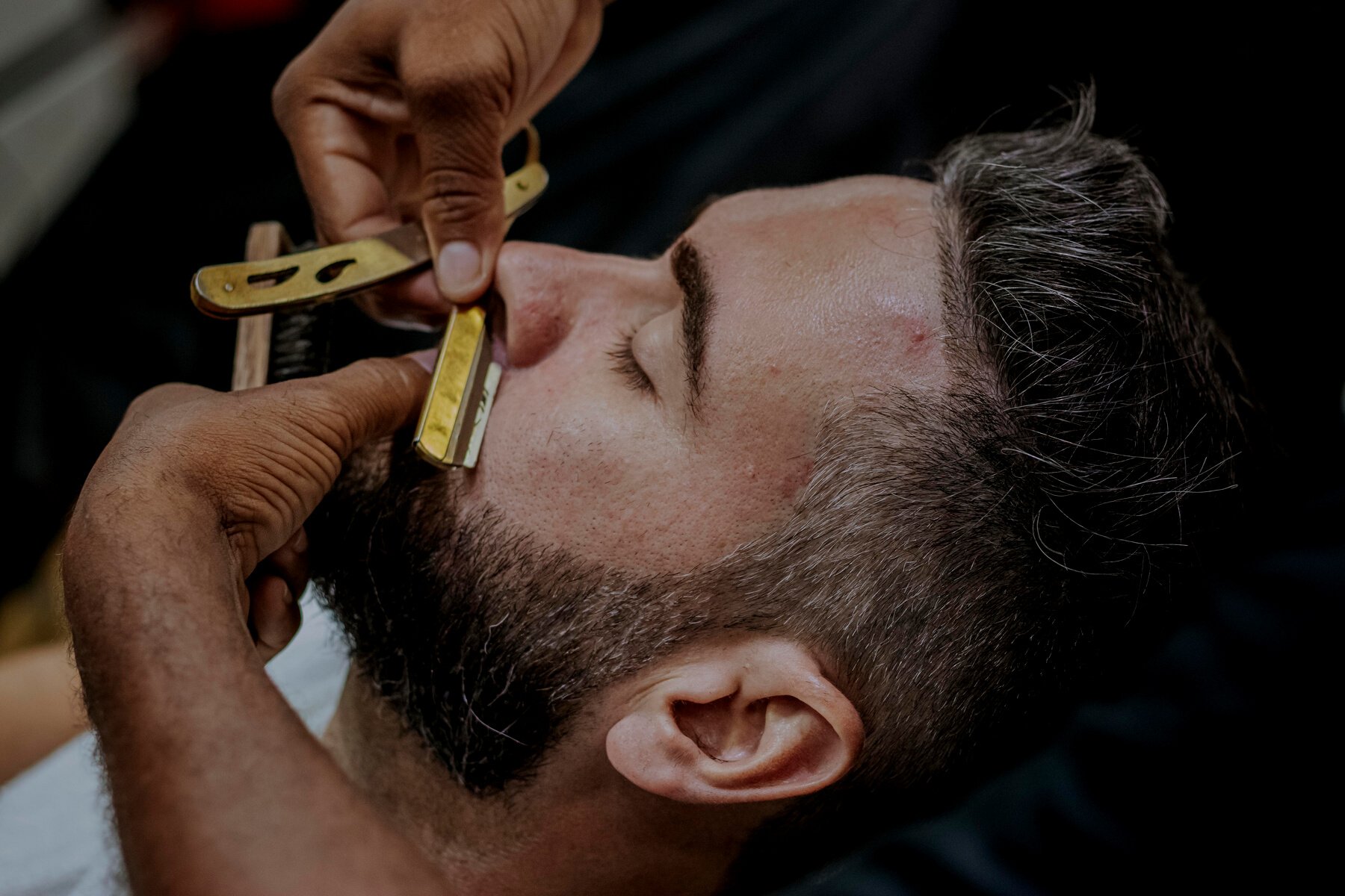 Person's Hands Using a Straight Razor to Shave a Man's Facial Hair