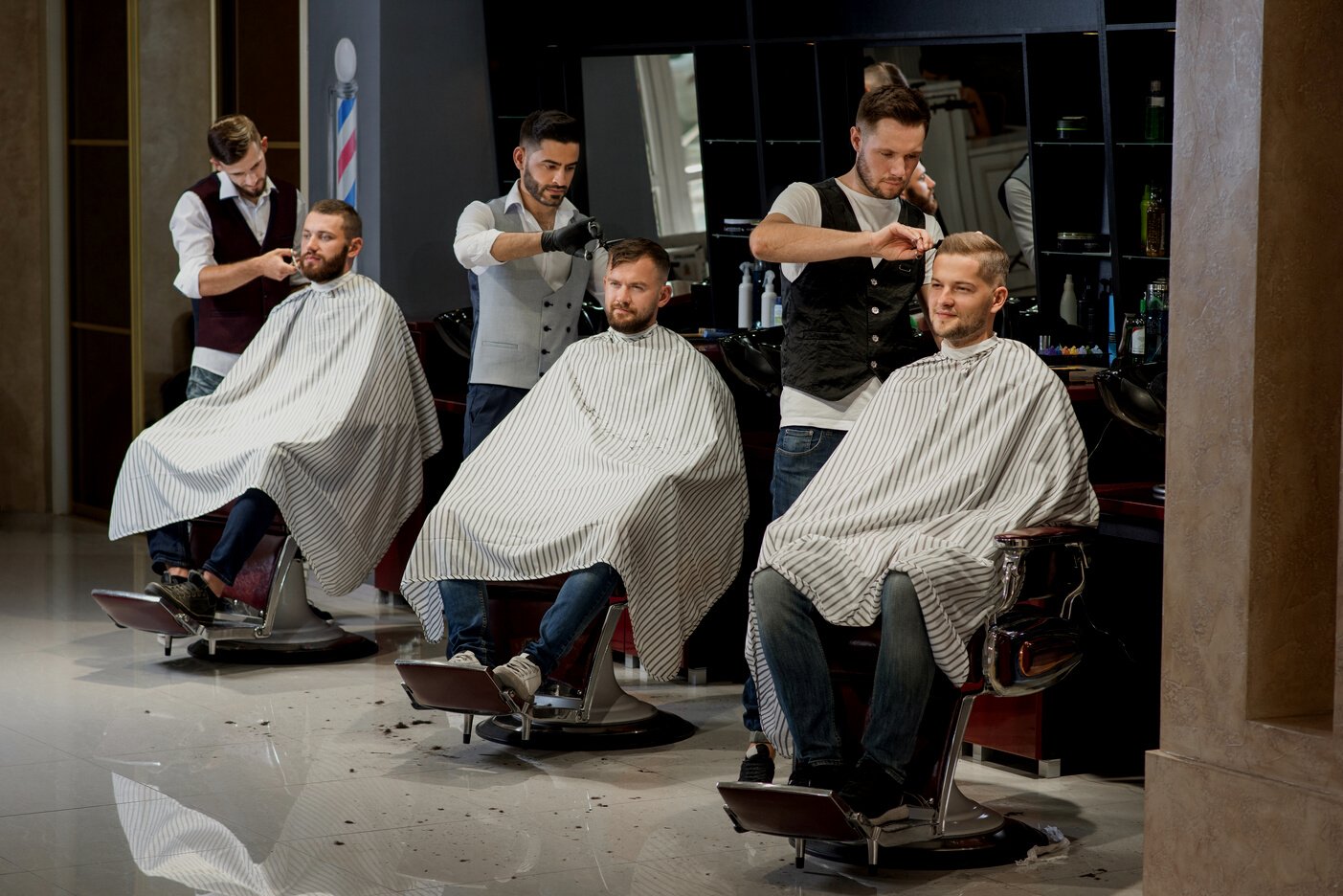 Barbers grooming and styling haircuts of clients in barbershop.